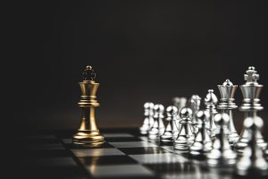 The Importance of Strategic Planning; A golden chess king stands isolated on a board, facing a group of silver pieces. The background is dark, creating a dramatic and tense atmosphere.