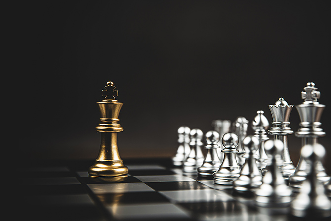 The Importance of Strategic Planning; A golden chess king stands isolated on a board, facing a group of silver pieces. The background is dark, creating a dramatic and tense atmosphere.